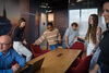 A group of people going to sit down at a long table for a meeting, they are happy.